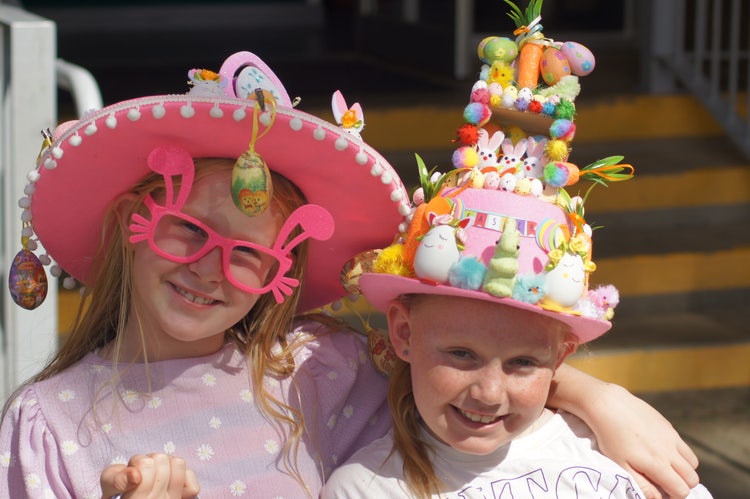 2 students smiling at the camera at our Easter hat parade. Their hats are covered in Easter eggs and rabbits